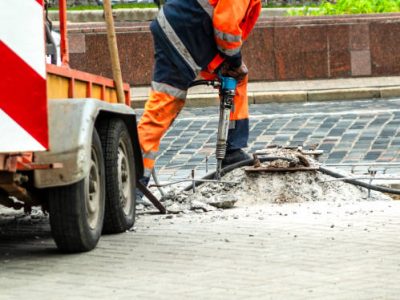 Male worker with full safety equipments drilling and repairing concrete driveway surface with jackhammer ,danger sign area.