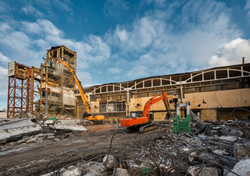 Contemporary hydraulic excavators with scissors and bucket work at demolition site of abandoned industrial complex buildings