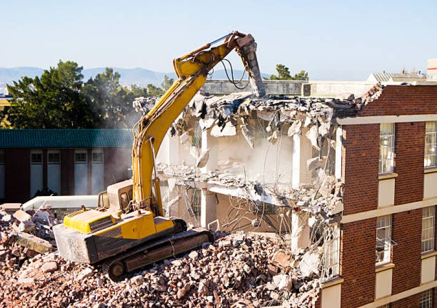 Demolition vehicle amid the dust and rubble of the wasteland it has created. On the end of its hydraulic arm is a powerful jackhammer.